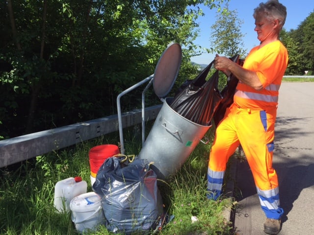 Mann in orangem Anzug vor Abfalleimer.