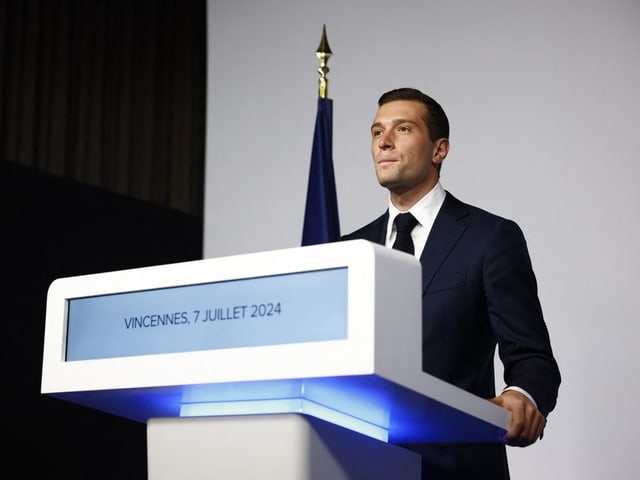 Mann im Anzug hält Rede hinter Podium in Vincennes.