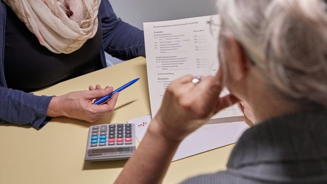 Zwei Personen schauen an einem Tisch auf ein Papier und einen Taschenrechner.