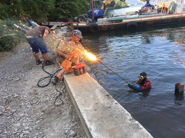 Mann entzündet einen Schweissstab, der von einem Taucher im Wasser gehalten wird.