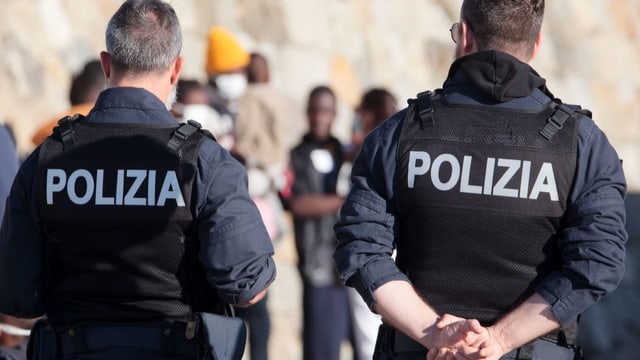 Italienische Polizisten vor Migranten, die aus Seenot gerettet wurden und in Kalabrien angelandet sind.