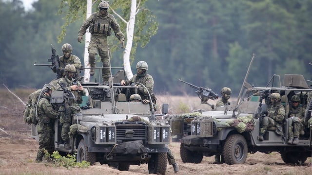 Soldaten in Tarnkleidung in und um mehrere Jeeps im Gelände.