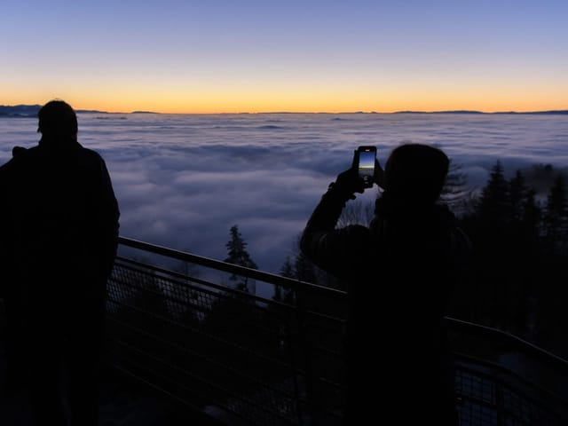 Menschen fotografieren Wolkenmeer bei Sonnenuntergang.