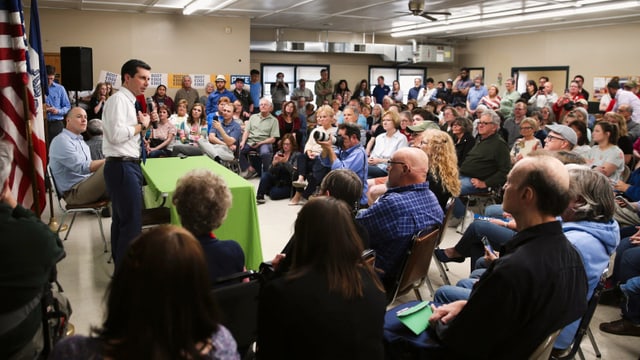 Buttigieg spricht zu Menschen in einem Saal.