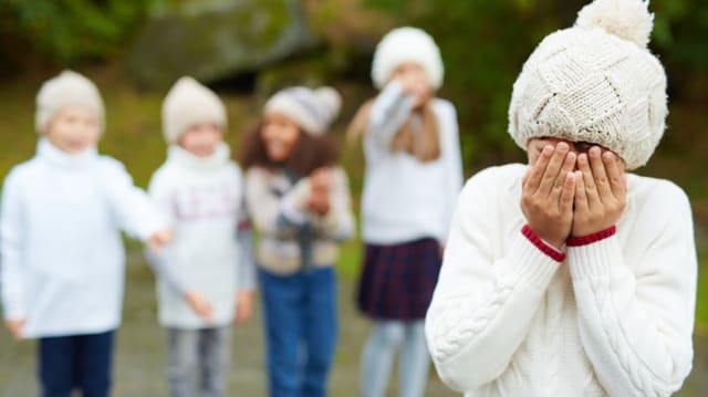 Vier Kinder deuten auf ein anderes Kind, das die Hände vor sein Gesicht hält