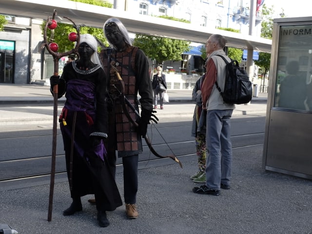 Ein junges Pärchen an der Haltestelle, Gesichter Schwarz bemalt.