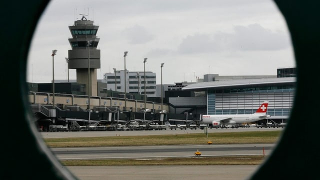 Durch ein rundes Loch blickt man auf den Kontrollturm aus Beton am Flughafen Zürich.