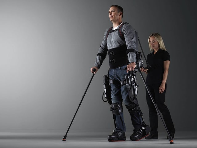 Mann in Exoskelett mit einer Person hinter sich