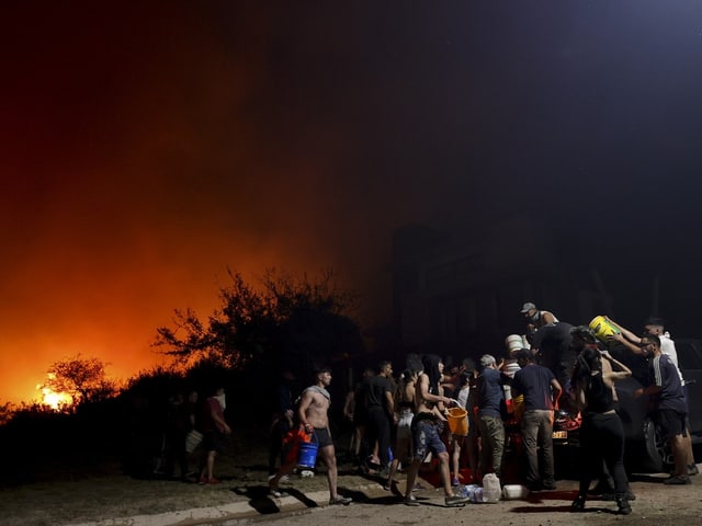 Ein Wald in Flammen. Nachbarinnen und Nachbarn helfen einander und tragen Behälter mit Wasser.