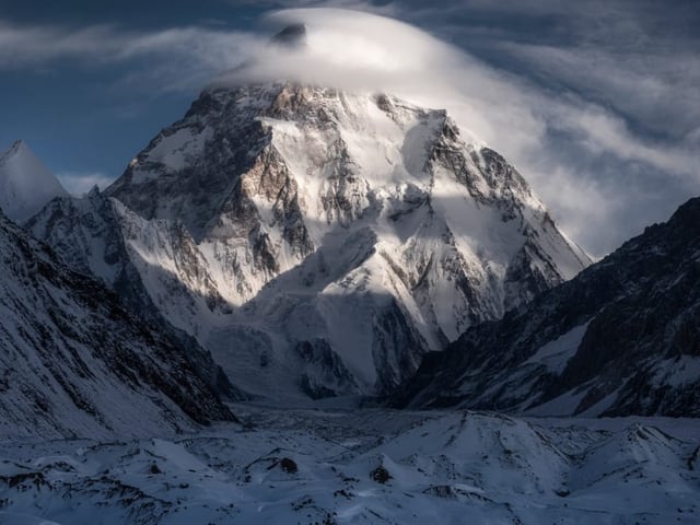 ein riesiger Gletscher, schneebedeckt ragt in den Himmel und durchstösst Wolken.