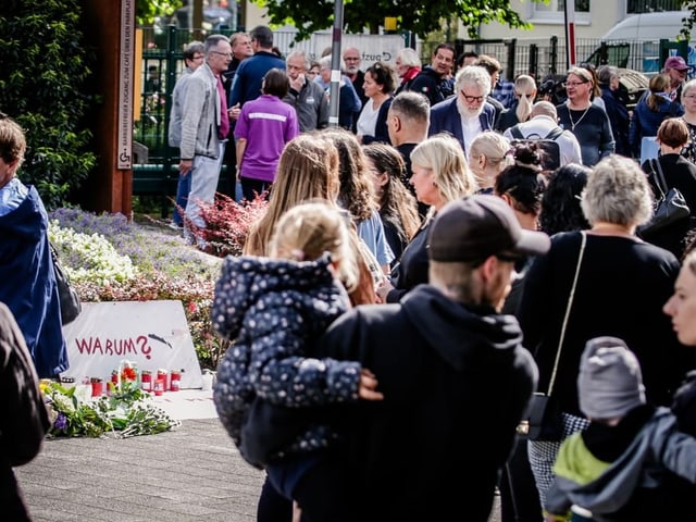 Menschenmenge versammelt sich bei einem Mahnmal mit Blumen und Kerzen.