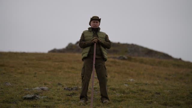 Putin in seinem Urlaub in der sibirischen Taiga auf einer grünen Ebene mit Stock.