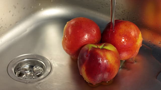 Drei Äpfel im Waschbecken unter dem Wasserstrahl.