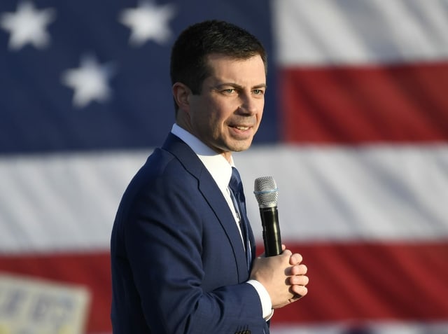 Pete Buttigieg mit Mikrofon vor einer USA-Flagge.