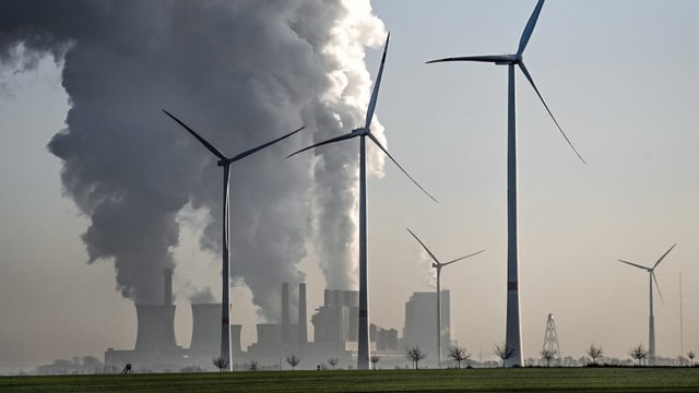 Im Vordergrund stehen Windräder. IM Hintergrund qualmt ein Krenkraftwerk.