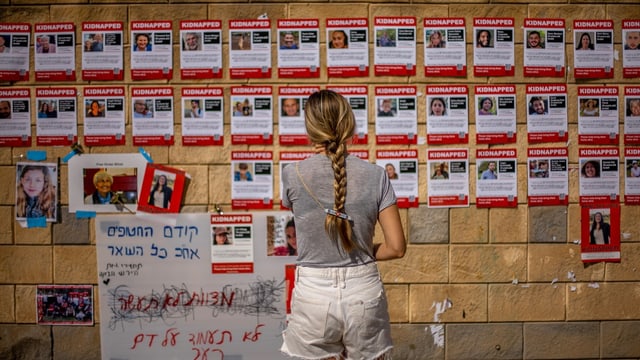 Eine Frau steht vor einer Wand mit Fotos von Vermissten.