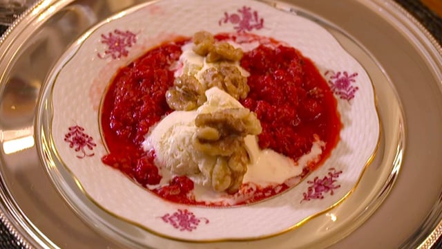 Ein Teller mit Vanilleglace, heissen Himbeeren und karamellisierten Baumnüssen.