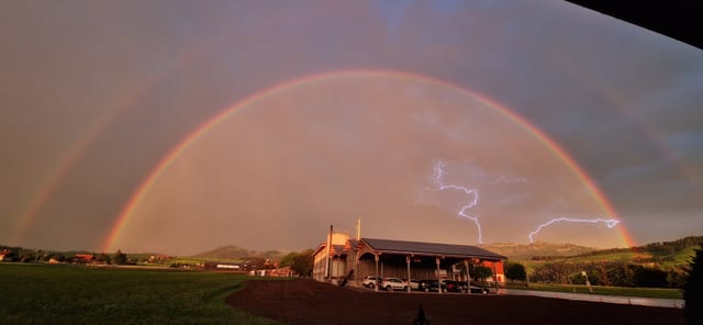 Regenbogen, dahinter zwei Blitze.