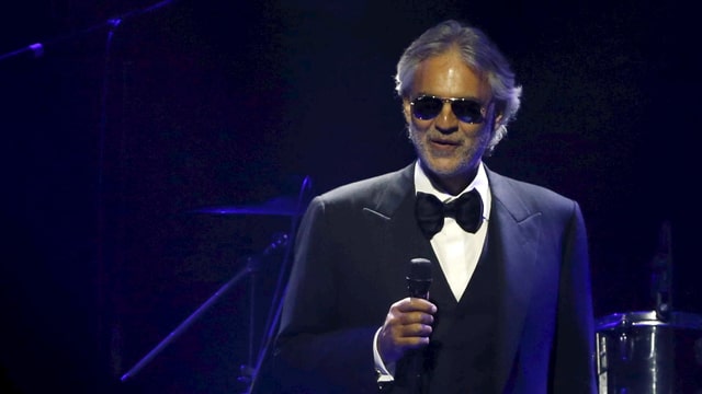 Andrea Bocelli im dunklen Anzug auf der Bühne.