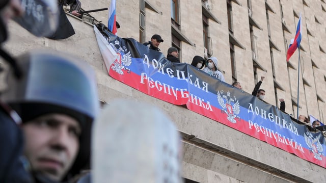 Vermummte Menschen mit russischen Flaggen auf einem Balkon.