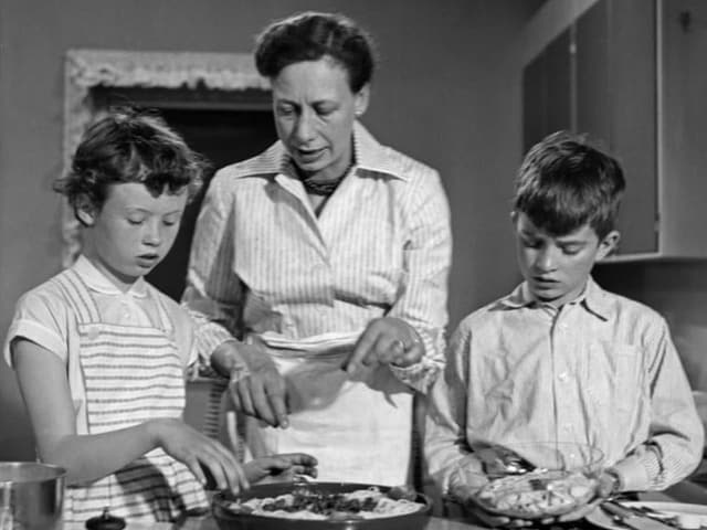 Eine Frau zeigt zwei Kindern beim Kochen.