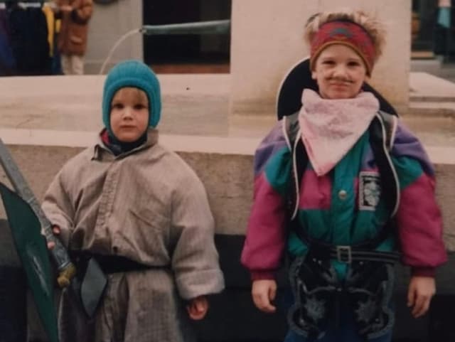 Zwei kleine Jungs stehen mit Stirnband und Kappe vor einem Brunnen.