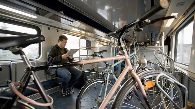 Eine Person sitzt in einem SBB-Wagen mit Velos.