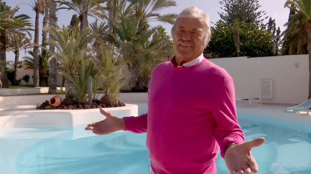 Hausi Leutenegger in einem pinken Pullover vor dem Pool im Garten seiner Villa.