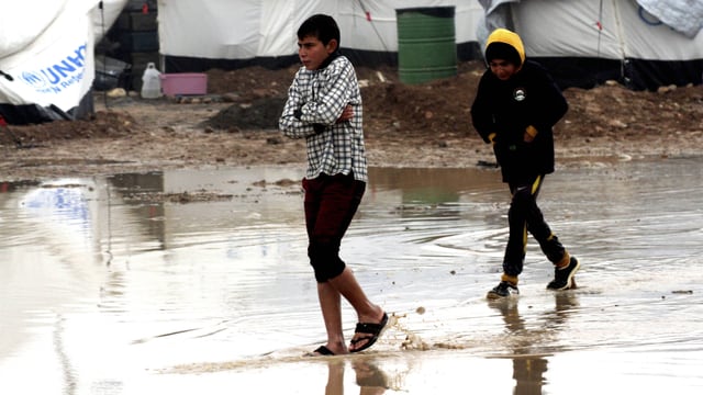 Zwei Knaben waten frierend durch eine riesige Pfütze in einem UNHCR-Flüchtlingslager.