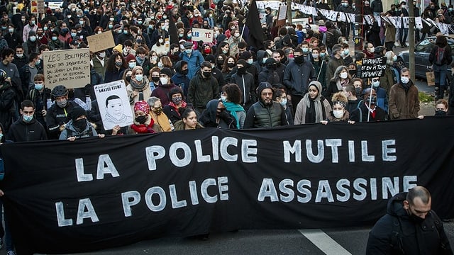 Protesters carry a banner.  It says in French: the police maim, the police kill.