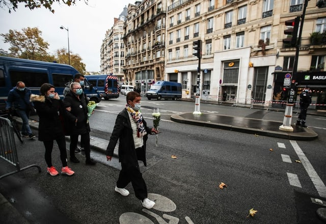 Vier Personen unterschiedlichen Alters tragen Blumen zum Konzertlokal Bataclan.