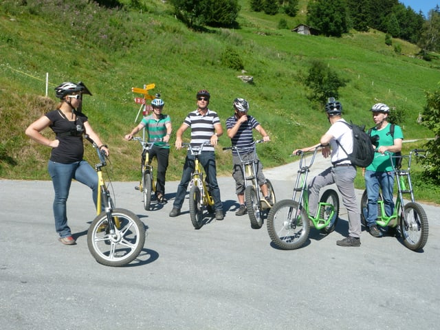 Sechs Personen stehen mit ihren Trottinetten an einer Weggabelung.