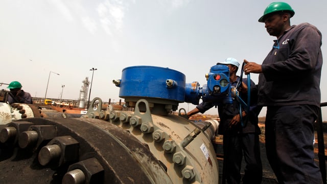 Zwei Arbeiter drehen an einem Rad an einer Ölpipeline im Sudan.