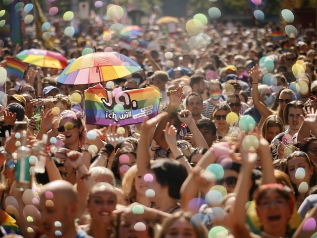 Menschen in einem Demonstrationszug. Man sieht Regenbogenfahnen.