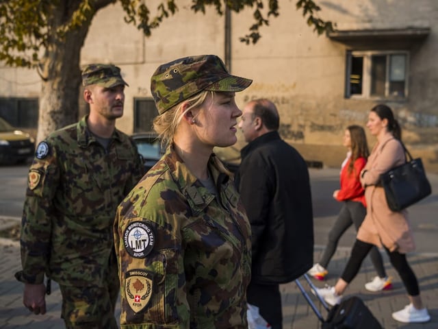 Zwei Soldaten in Tarnkleidung gehen auf einer Strasse.