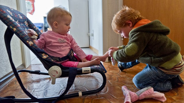 Ein kleines Kind zieht einem Baby Socken an.