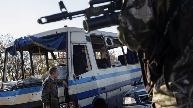 Pro-russische Rebellen an einem Checkpoint, einer mit Maschinengewehr, der andere lehnt an einen Bus.