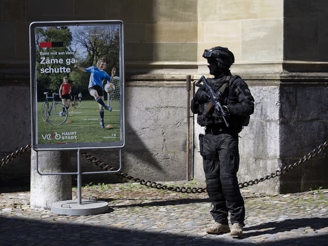 Total vermummter Soldat mit Sturmgewehr steht in einer Ecke.