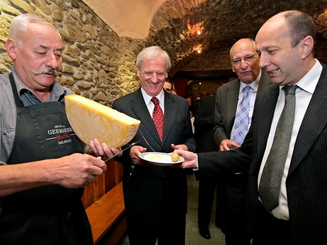 Vier Personen in einem Weinkeller. Eine streicht eine Portion Raclette auf den Teller.