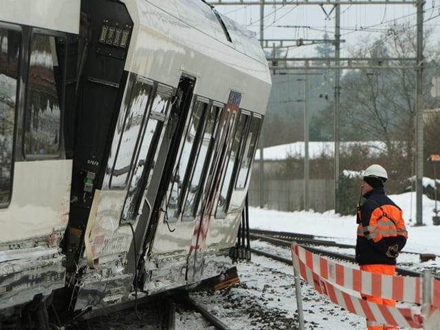 Bahnarbeiter neben einem entgleisten Bahnwaggon.