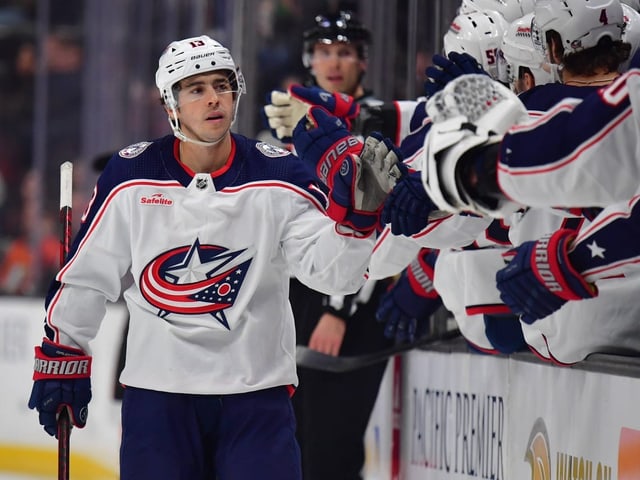 Eishockeyspieler im Columbus Blue Jackets Trikot klatscht mit Teamkollegen ab.