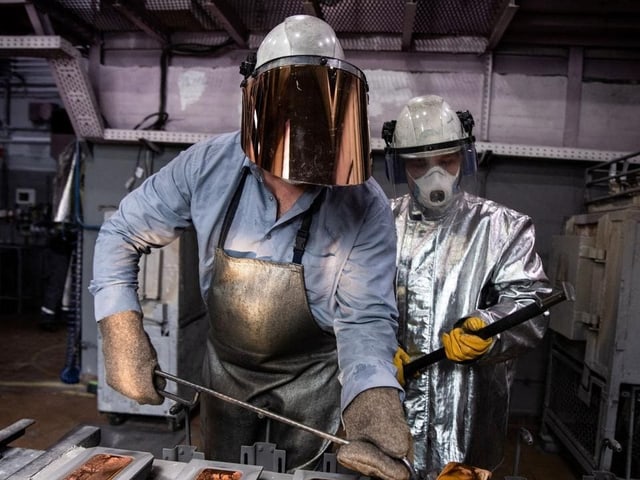 Zwei Arbeiter in Schutzanzügen und Helmen in einer Fabrik.