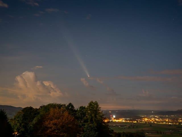 Nachtlandschaft mit Komet über beleuchteter Stadt.