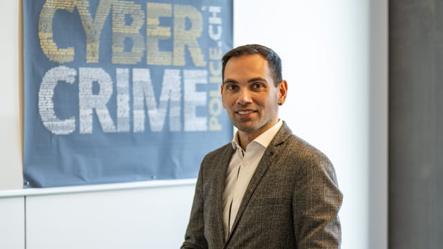 Ein Mann mit kurzen Haaren und im Anzug. Im Hintergrund ein Poster mit der Aufschrift «Cybercrime, Police.ch»