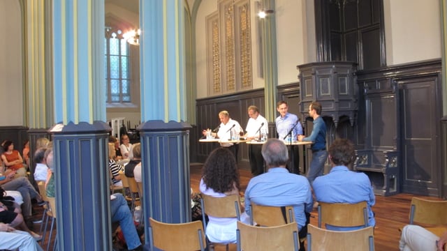 Vier Männer vor Publikum in einem Kirchenraum