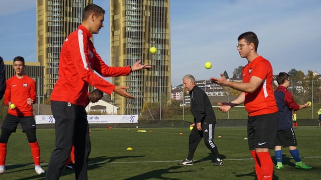 Zwei Fussballspieler werfen sich kleine Bälle zu.