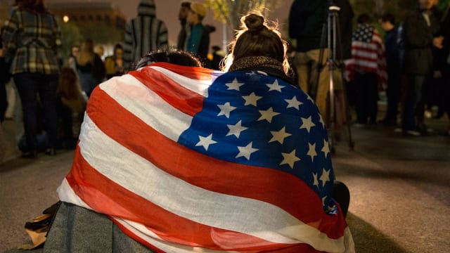 Ein Paar sitzt auf der Strasse, eng eingewickelt in eine USA-Flagge.