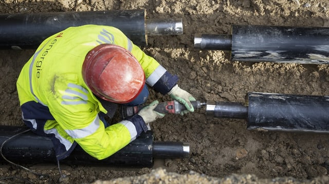 Arbeiter verlegen Fernwaermeleitungen auf einer Baustelle in einem Wohnquartier.