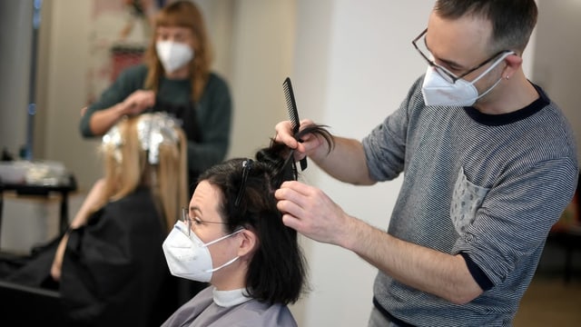 Coiffeur schneidet Frau die Haare. Beide tragen Maske.