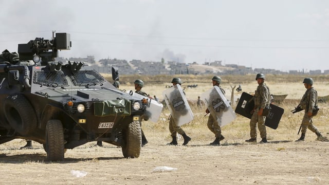 Türkische Soldaten mit Plexiglas-Schutzschilden gehen auf ein gepanzertes Militärfahrzeug zu.